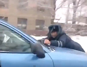 A Irkutsk ladruncolo trascina un poliziotto sul cofano della macchina